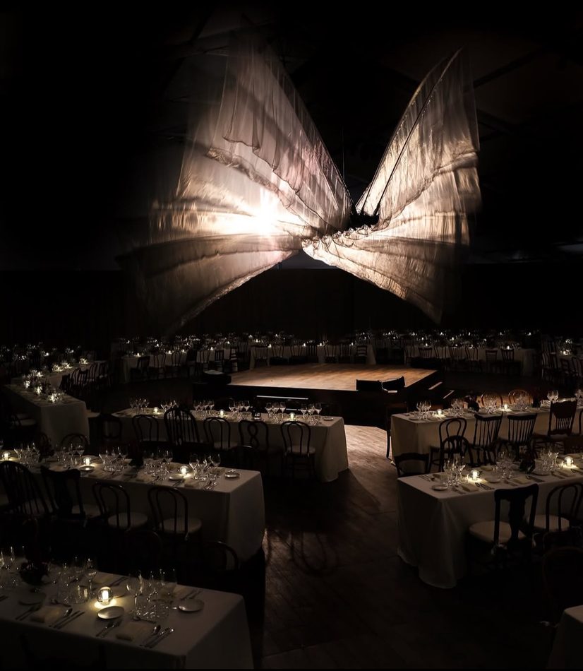 Dramatic tent lighting installation glowing over a formal dinner setup at night