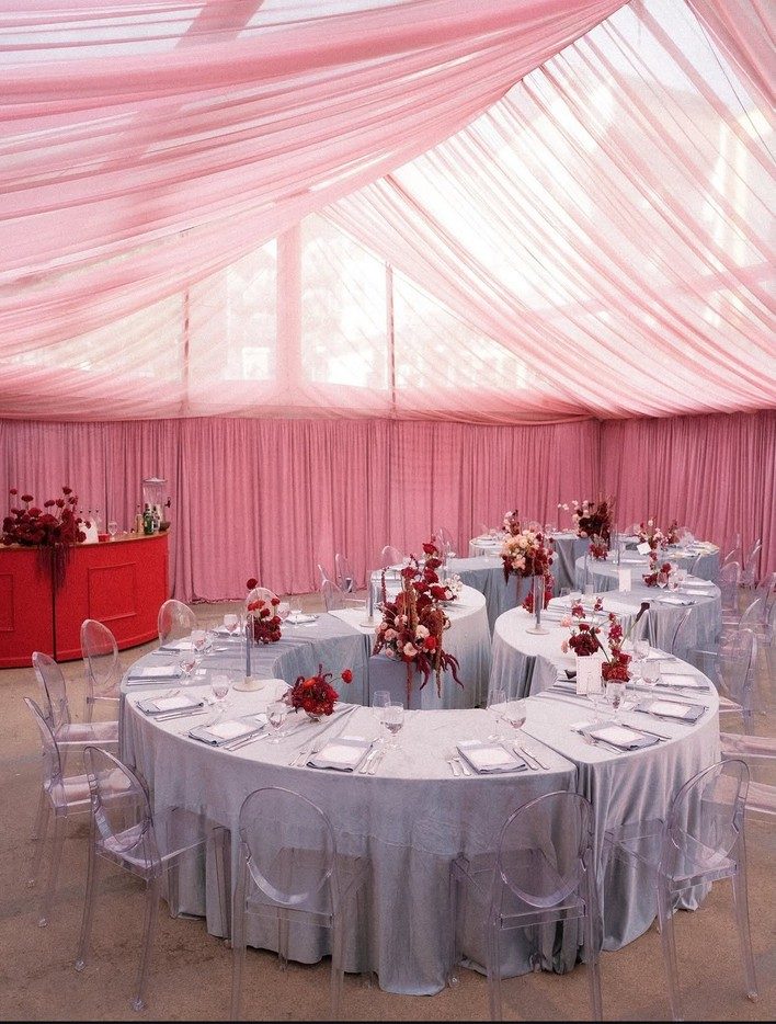 Round tables with pink linens set beneath pink draped tent ceiling